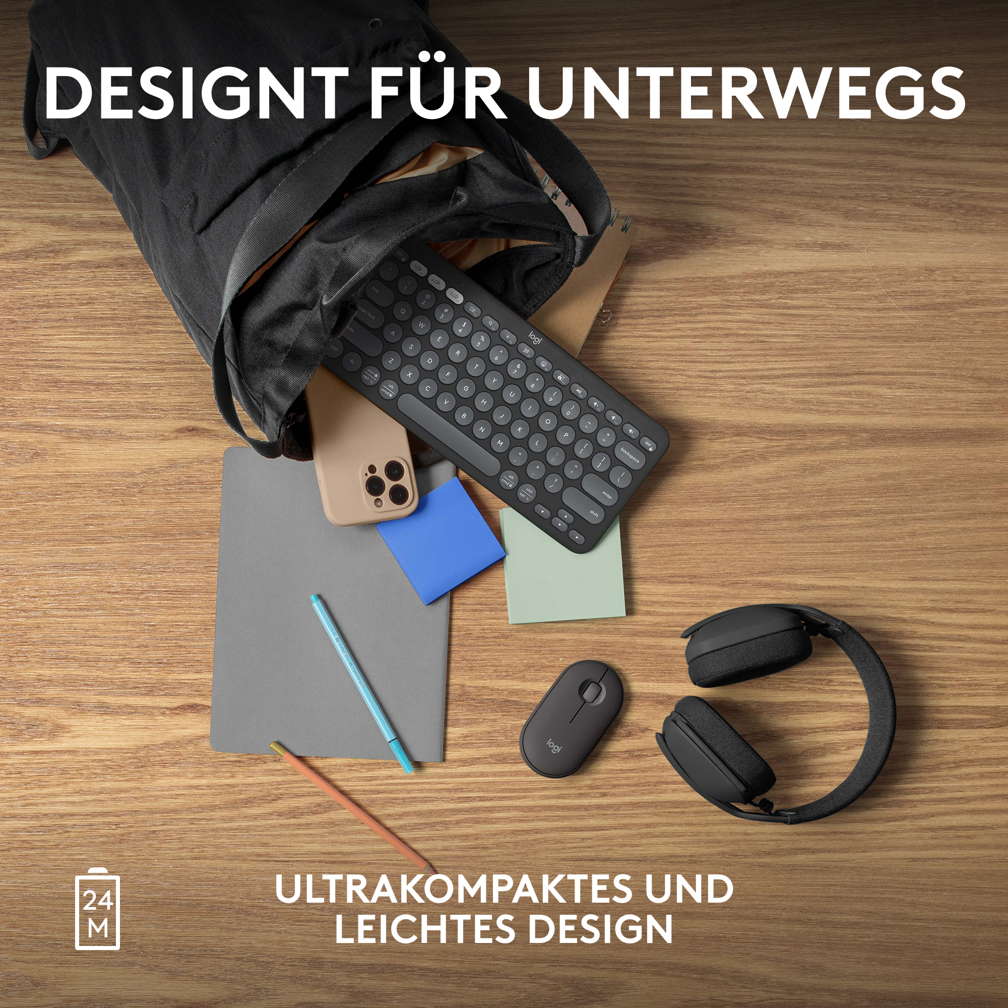 Eine schwarze Tastatur, Kopfhörer, Maus, Telefon und Notizblock auf einem Holztisch.