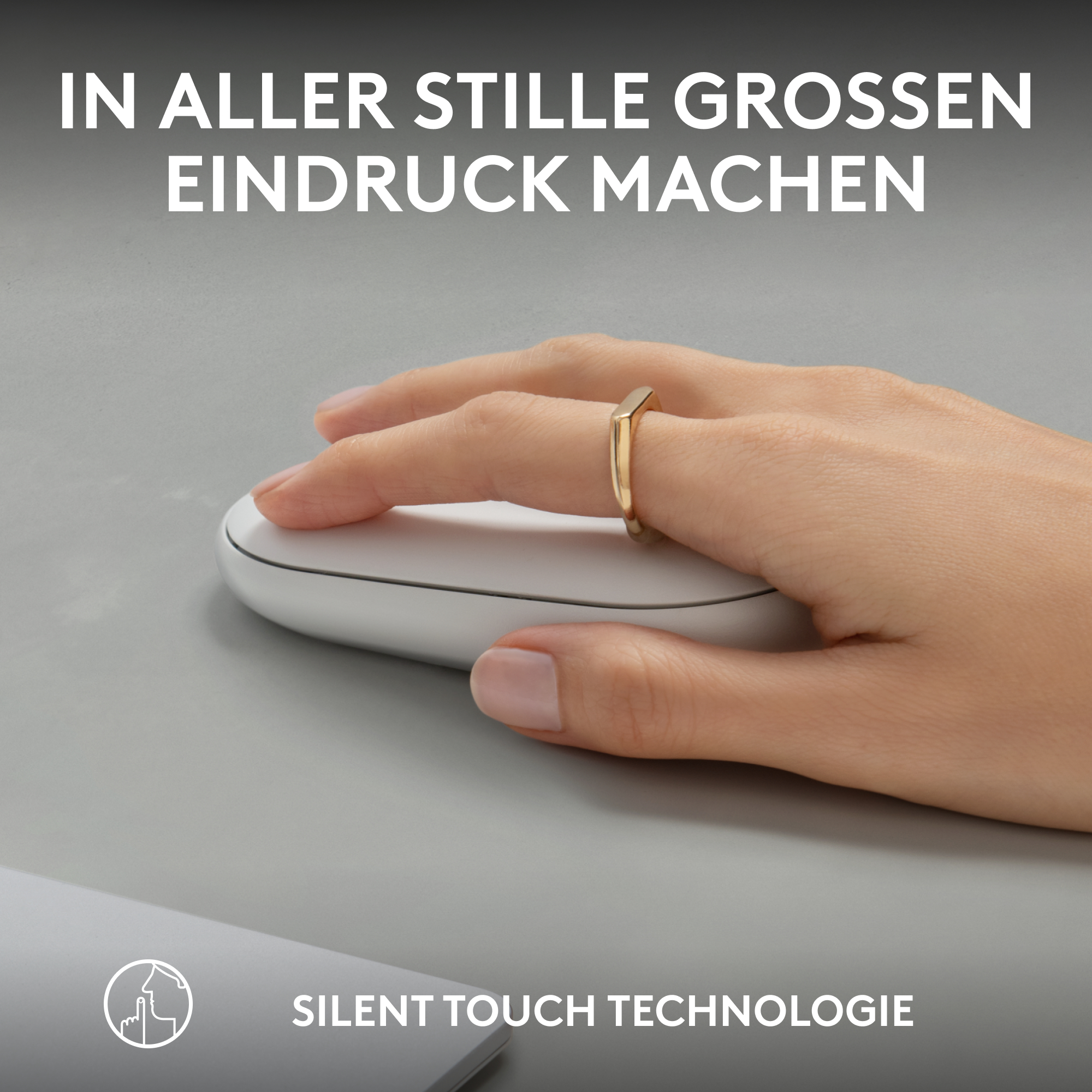 Hand mit goldenem Ring auf weißer Maus auf grauer Oberfläche. Text: 'SILENT TOUCH TECHNOLOGY'.