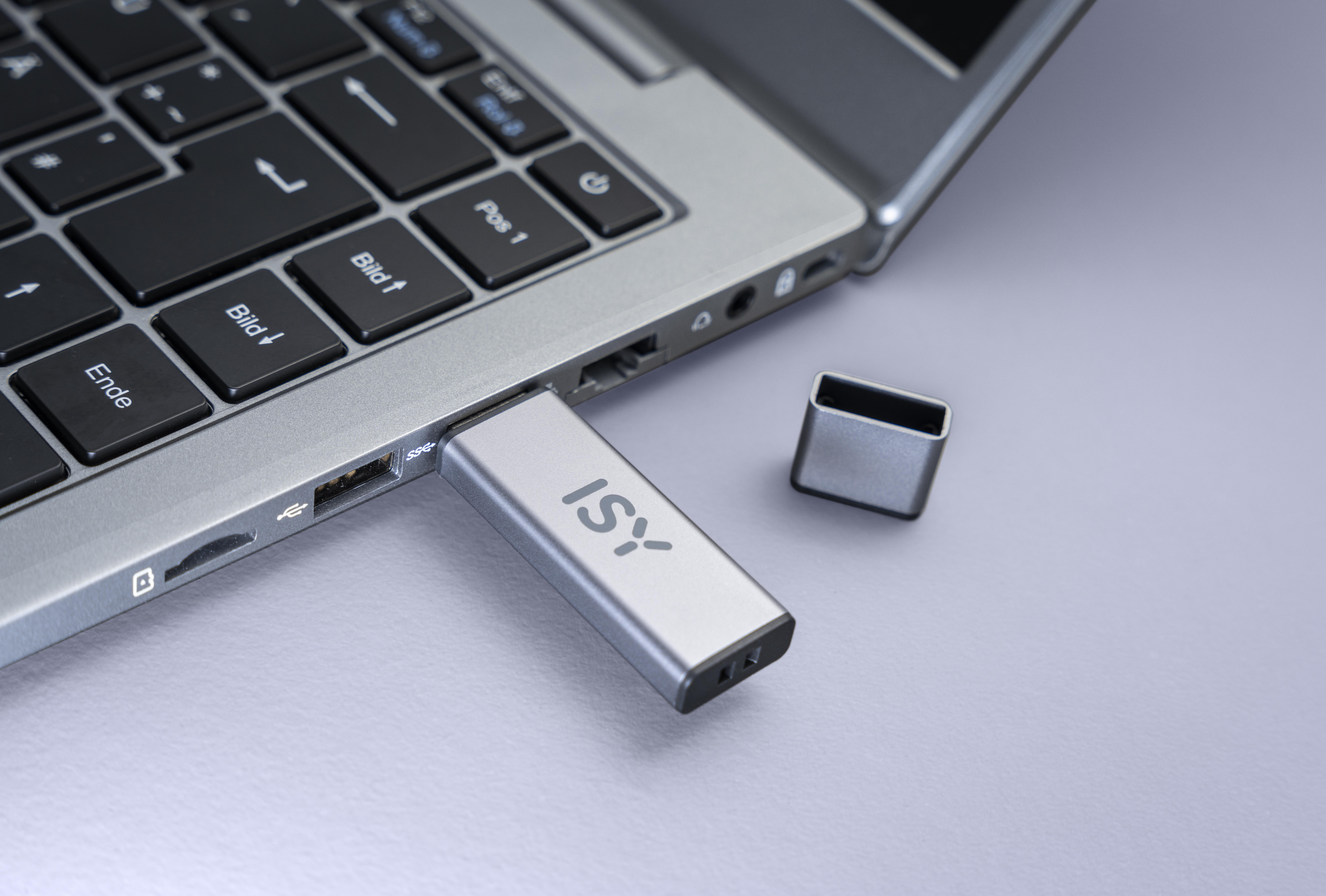 Ein silberner ISY USB-Stick, der in einen Laptop eingesteckt ist, mit der Kappe daneben.