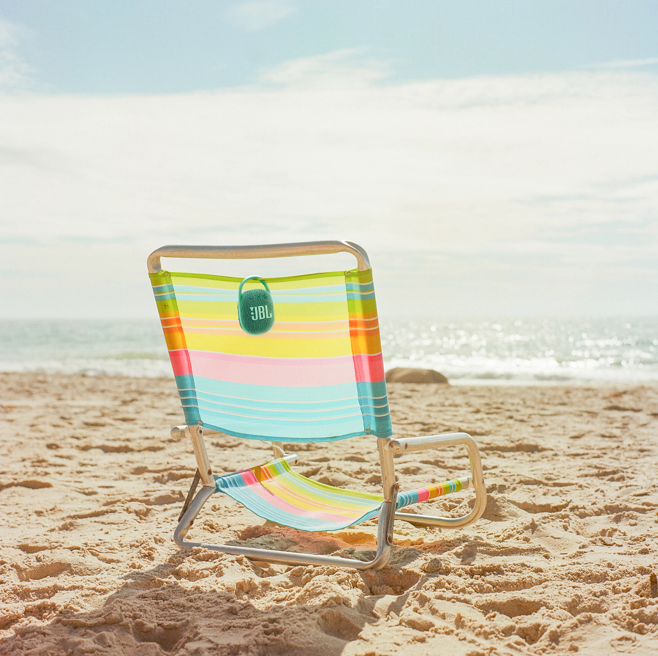Ein Strandstuhl mit Lautsprecher an einem Sandstrand, mit Meer und Himmel im Hintergrund.