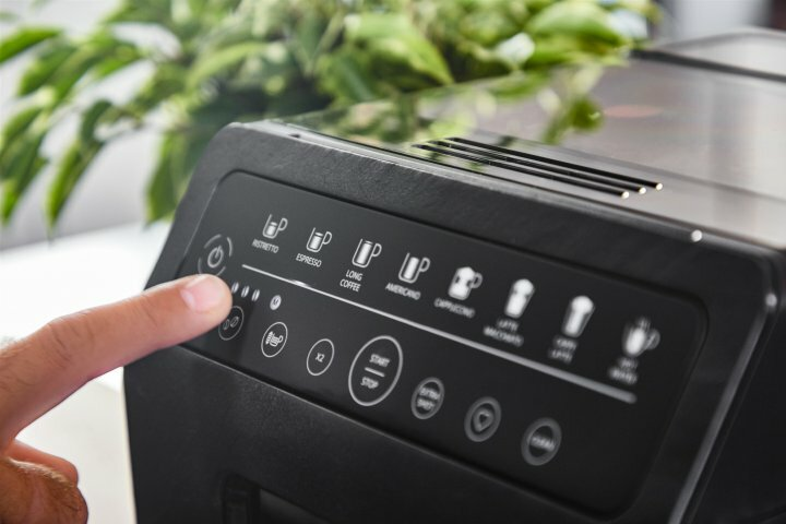 Ręka naciskająca przycisk zasilania na panelu sterowania czarnego ekspresu do kawy z różnymi ikonami.