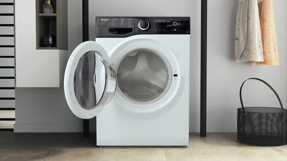 Biała pralka z otwartymi drzwiami stoi na podłodze wyłożonej kafelkami.