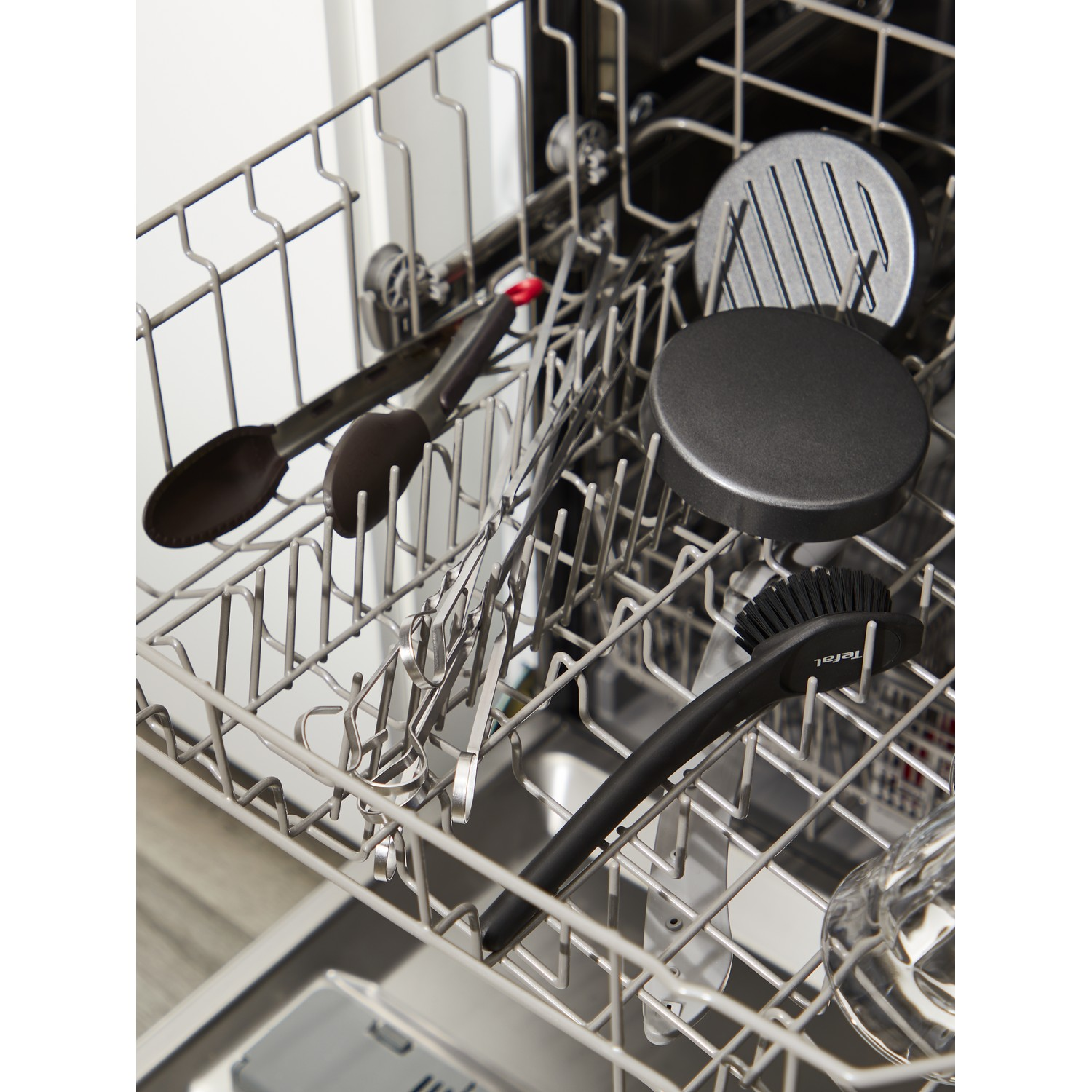 Dishwasher rack with kitchen utensils, including tongs and a brush.