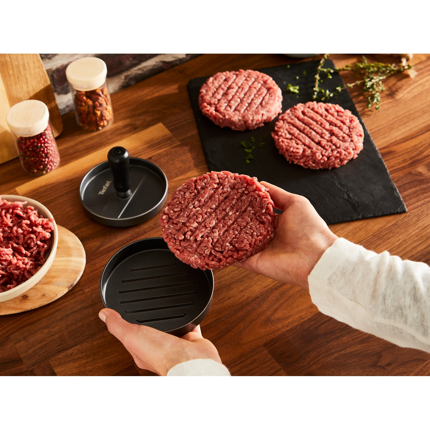 A person forming burger patties with a Tefal burger press on a wooden surface.
