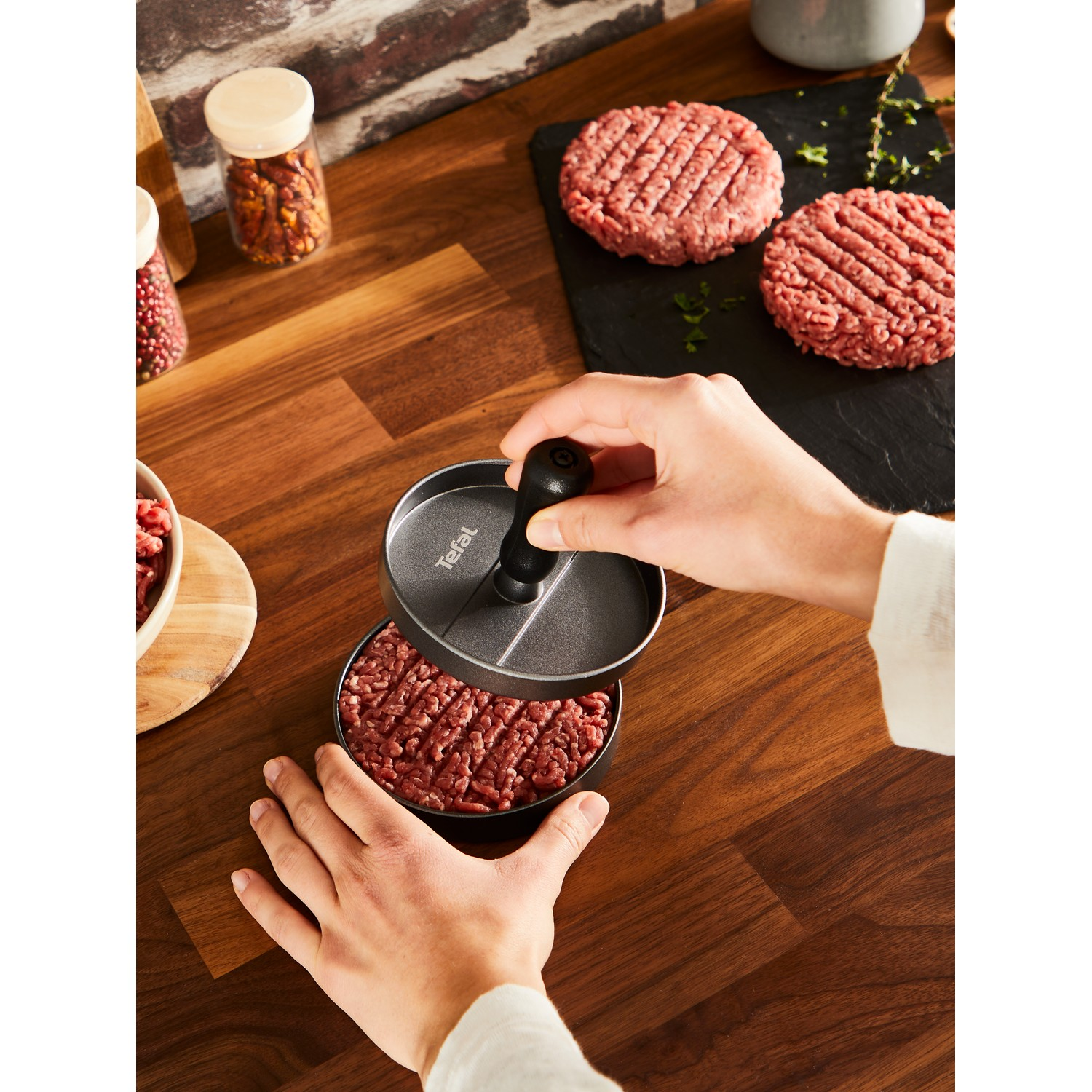 Hands pressing ground beef into a burger patty. A black Tefal burger press is used.