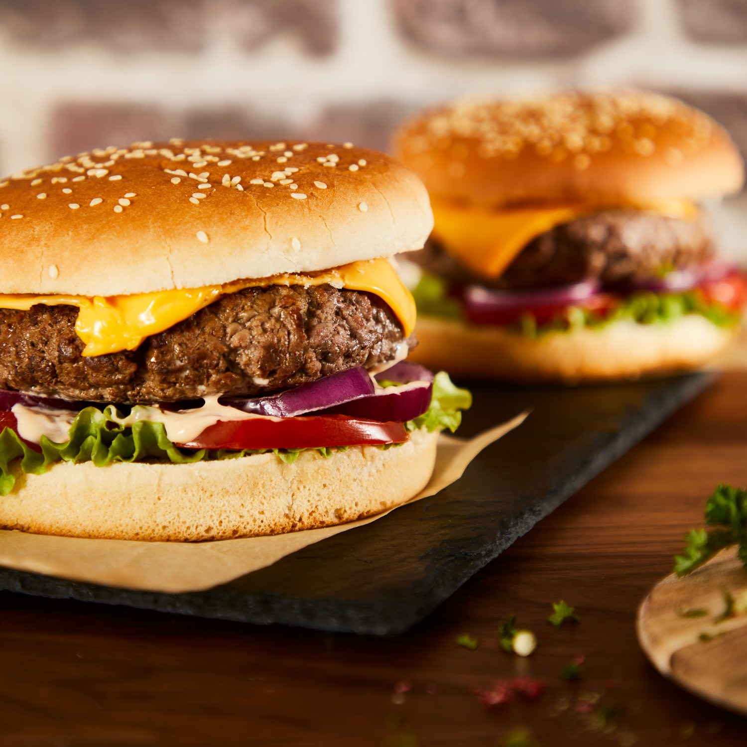 Two burgers on a dark surface with lettuce, tomatoes, cheese, and sesame buns.