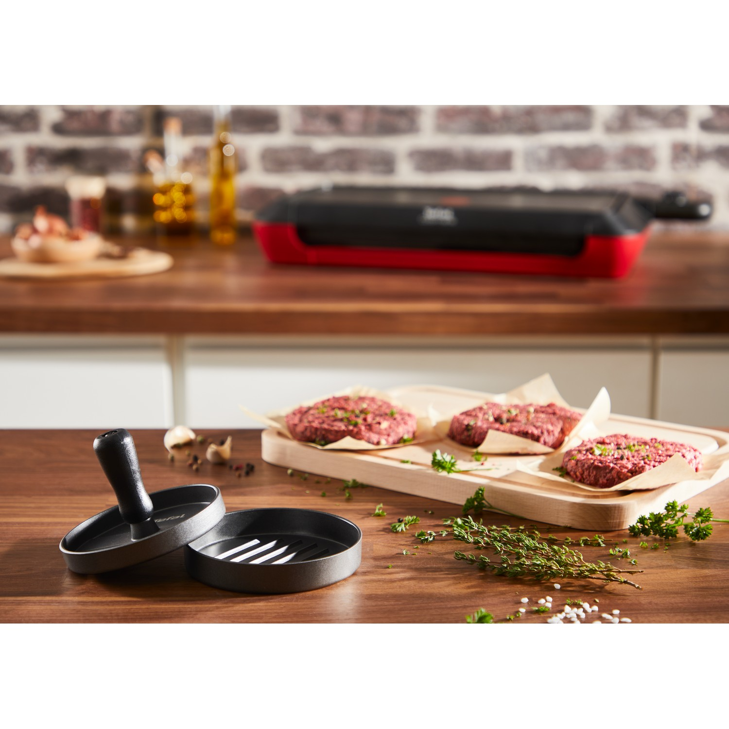 Burgers on paper, press, thyme, parsley, and a grill in the background.