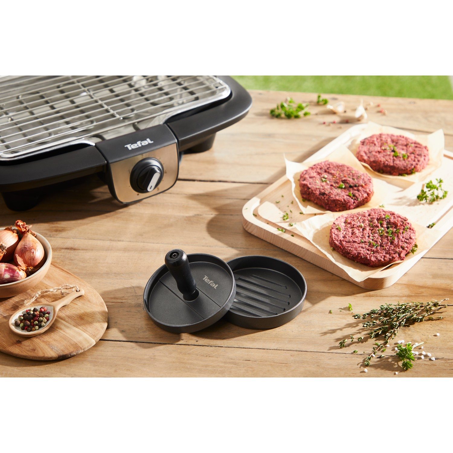 A grilling setup with burgers and burger press on a wooden table.