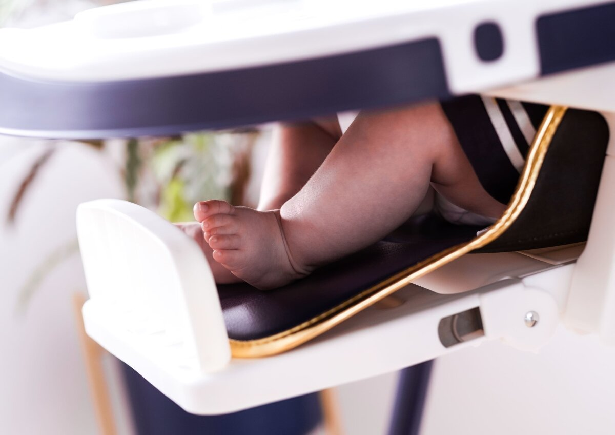 Stopy dziecka w krzesełku do karmienia, na niebieskim siedzisku.
