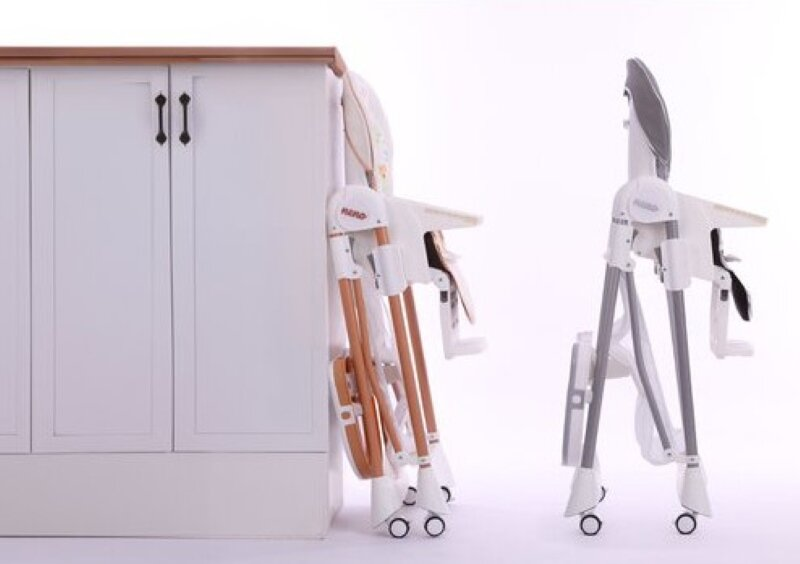 Złożone krzesełko do karmienia. Jedno złożone, jedno stojące. Białe szafki w tle.