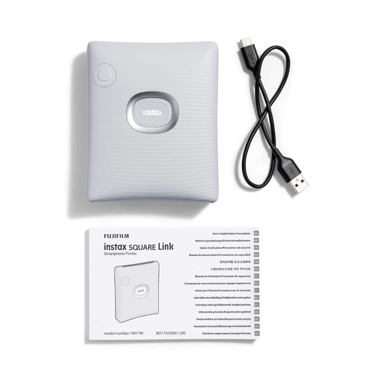 White Instax printer, USB cable, and a manual on a dark background.