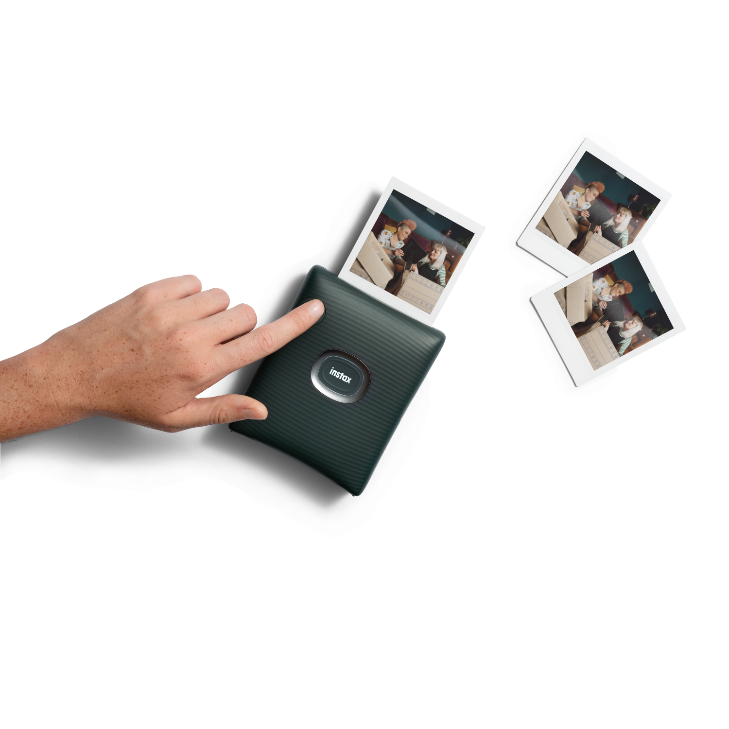 Een hand drukt op een knop van een donkergroene Instax-printer, die een foto uitwerpt.
