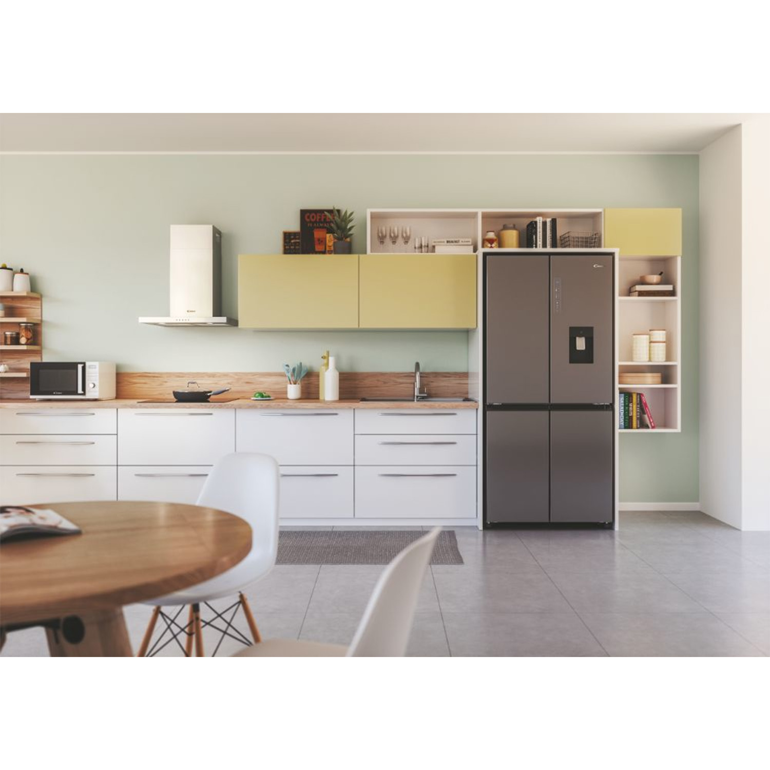 Cucina con mobili bianchi, un frigorifero e un tavolo rotondo in legno con sedie.