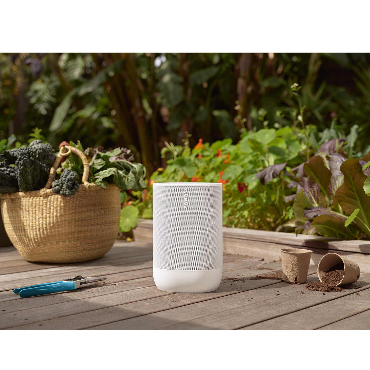 Altoparlante bianco in un ambiente giardino. Piante e una terrazza in legno sullo sfondo.