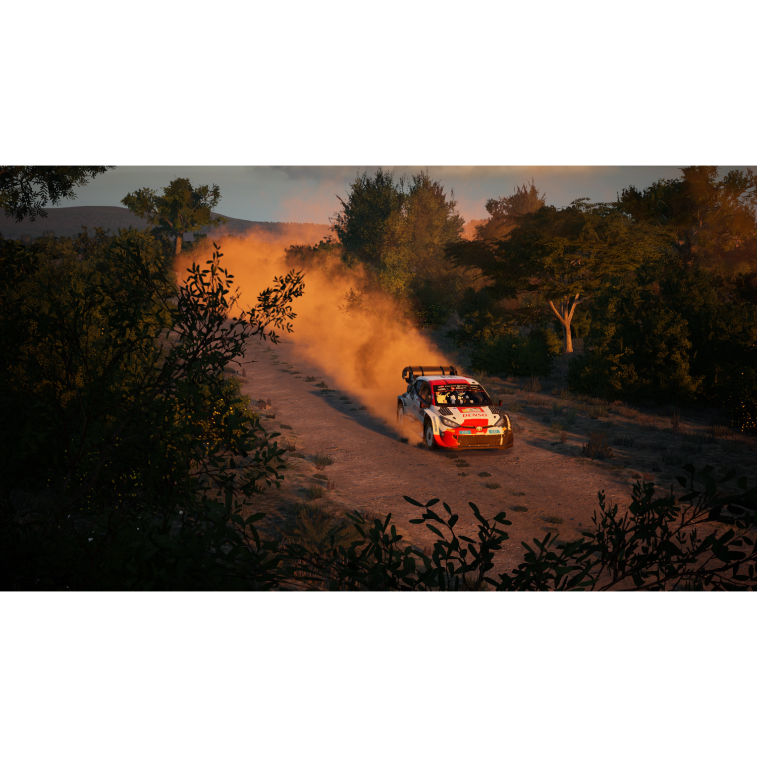 Een rallyauto scheurt over een onverharde weg, waarbij stof opwaait, te midden van groene bomen en een gouden zonsondergang.