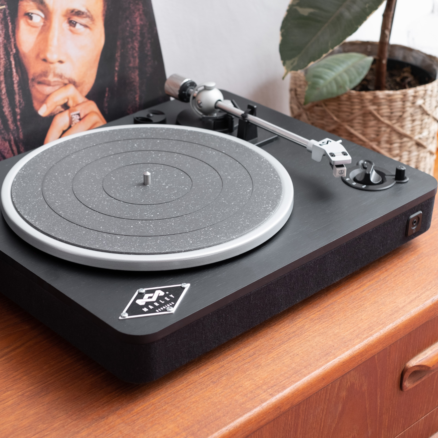 A black turntable with a vinyl record and a Bob Marley album cover in the background.