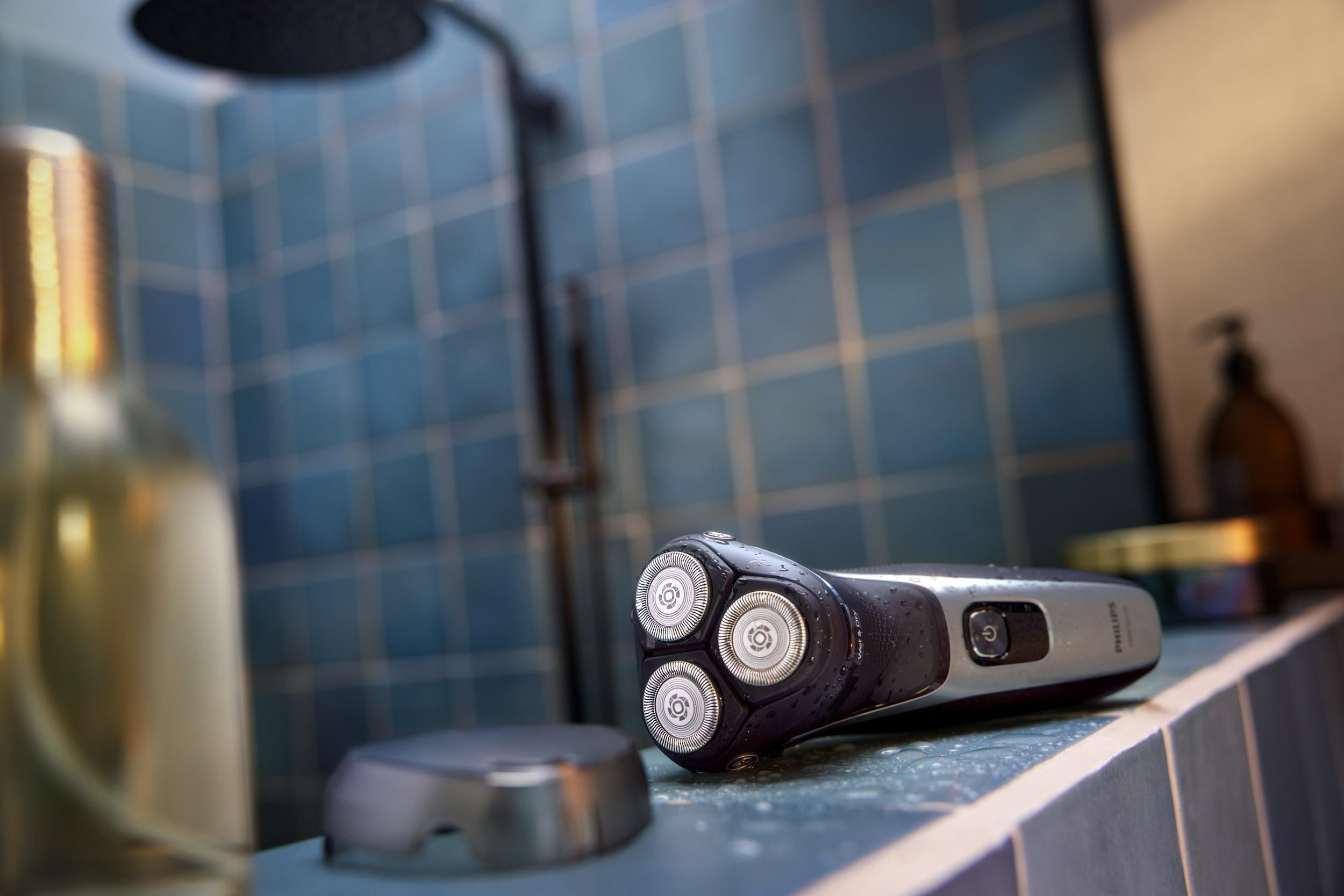 Elektrischer Rasierer auf einem Vorsprung in der Dusche, mit Duschkopf.
