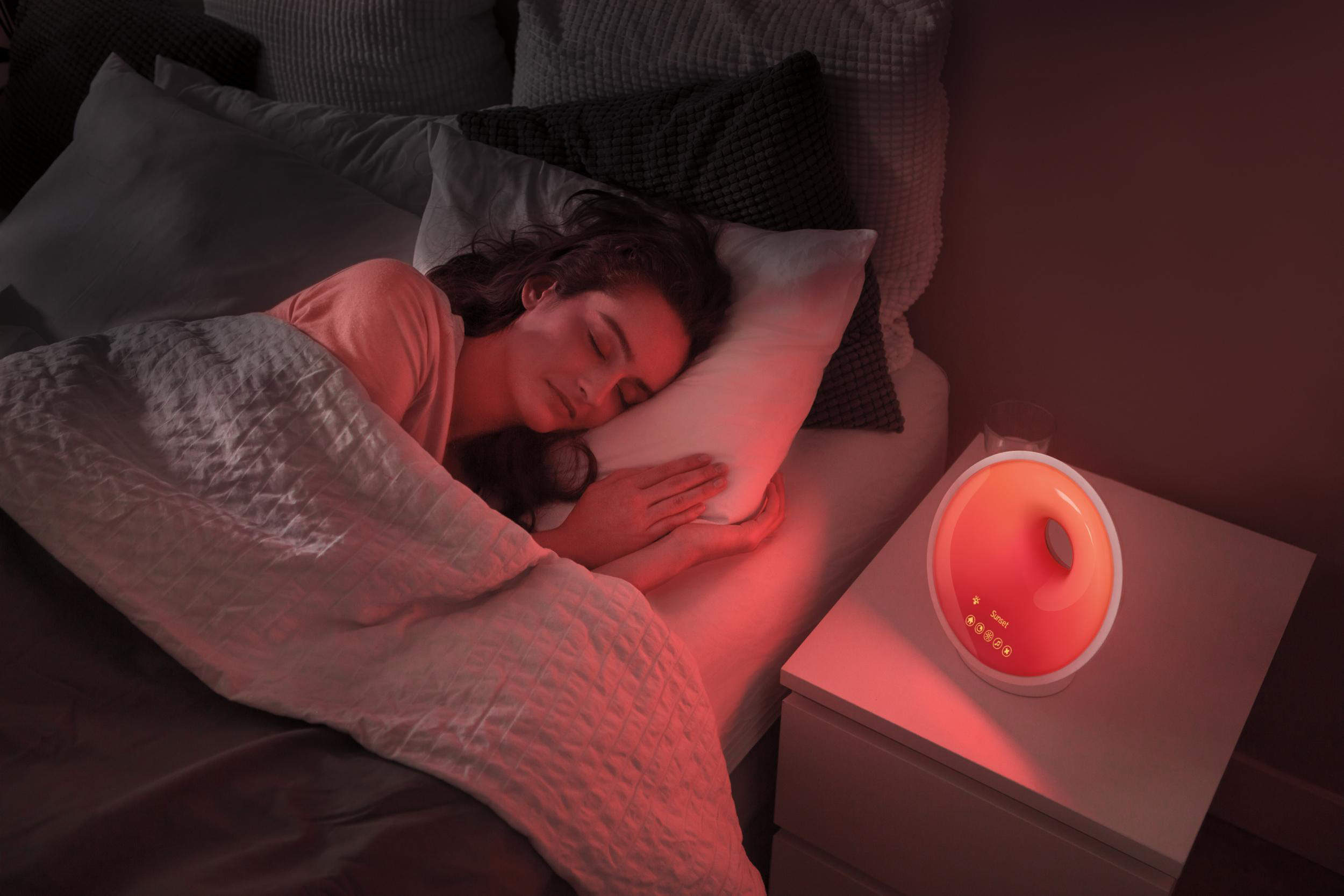 Eine Frau schläft im Bett mit einem rot beleuchteten Wecker auf dem Nachttisch.