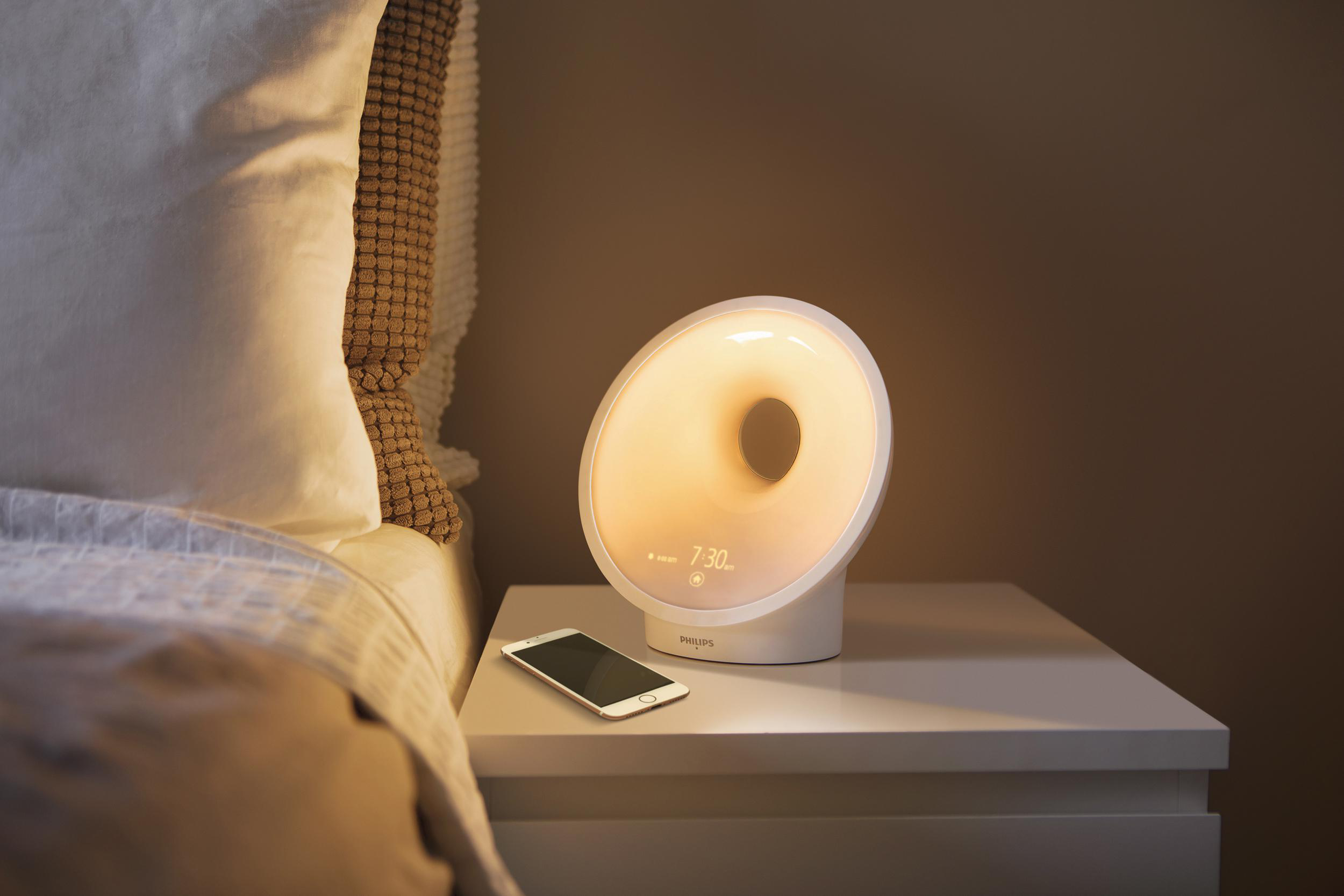 Ein Nachttisch mit einem leuchtenden Philips Wecker und einem Smartphone.