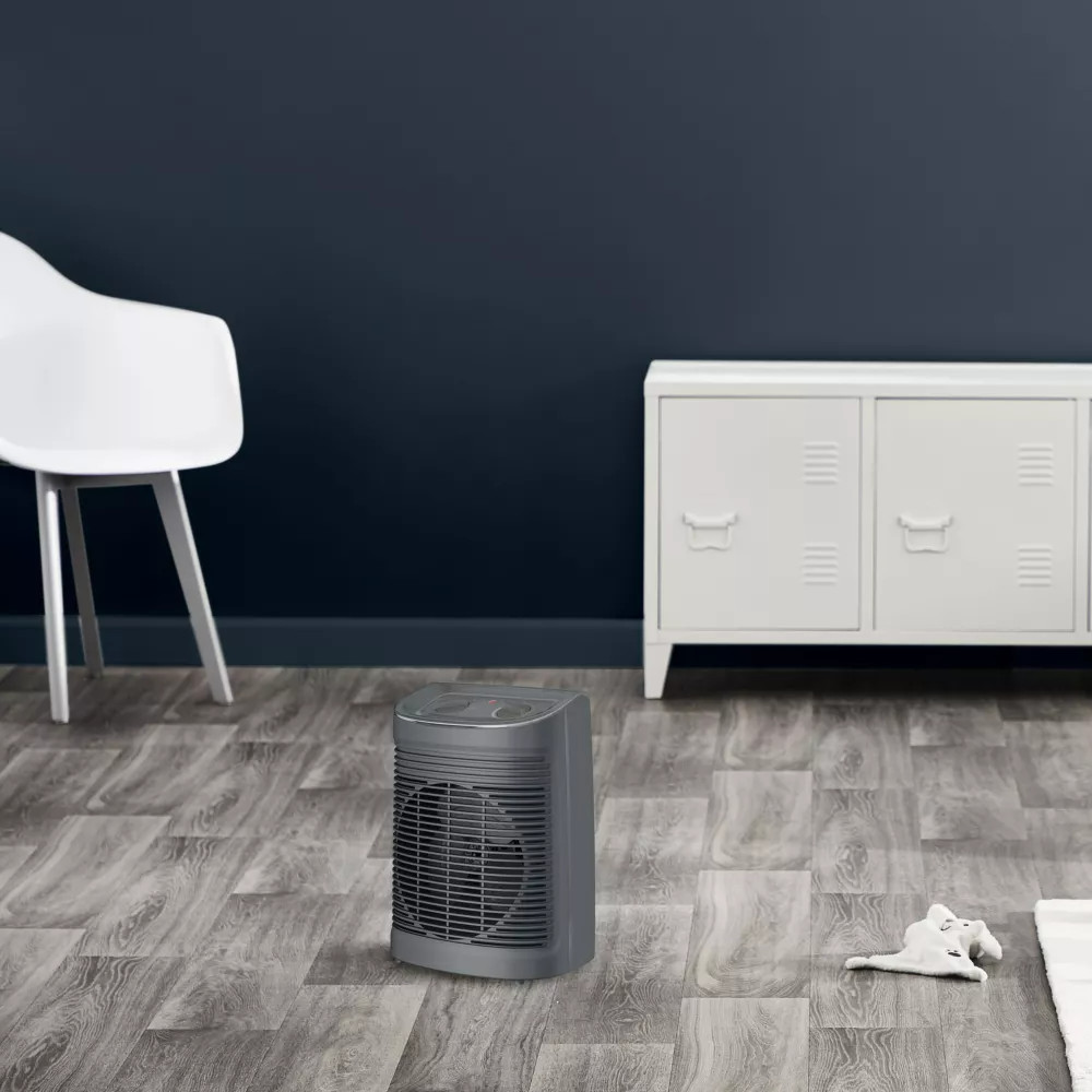 A gray electric heater on a wooden floor against a dark blue wall. White chair.