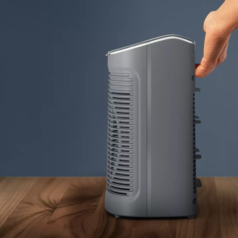 A grey air purifier on a wooden surface, hand touching side.