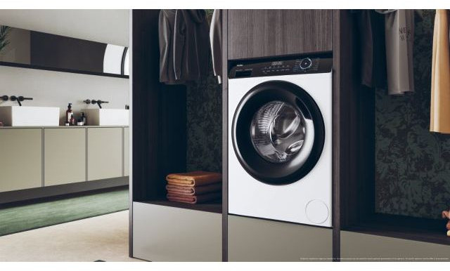 Wasmachine in kast. Witte voorkant met zwarte deur. Kast met kleding en handdoeken.