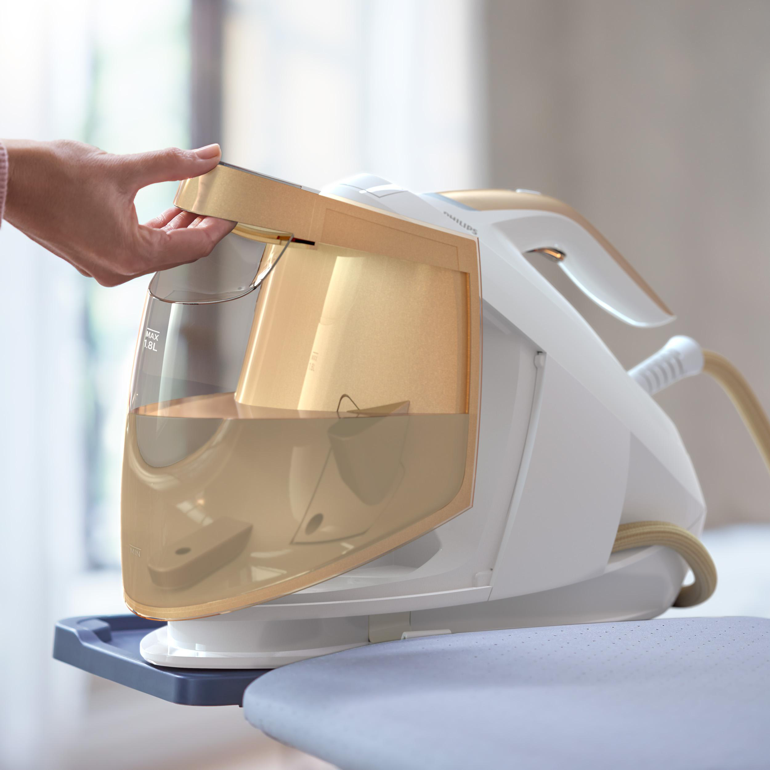 Weißes und goldenes Bügeleisen mit Wassertank, der von einer Hand geöffnet wird.