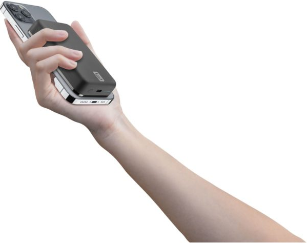 Une main tient une batterie externe noire à côté d'un téléphone. Le téléphone est argenté et le fond est blanc.