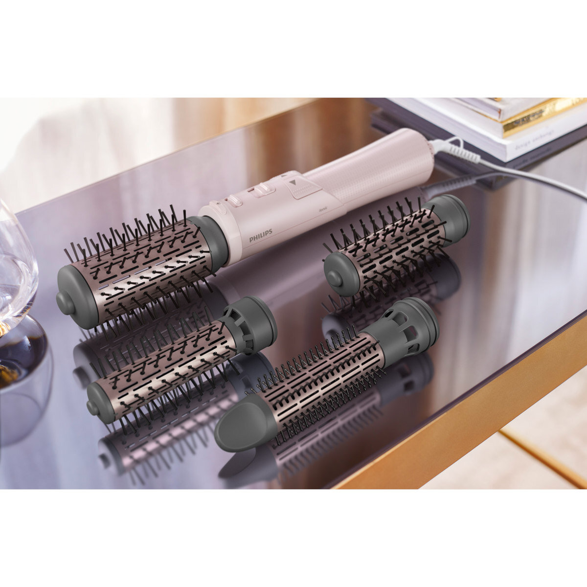 Narzędzia do stylizacji włosów: głowica szczotki, różowy uchwyt i różne nakładki na szczotkę na odblaskowej powierzchni.