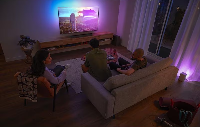 Trois personnes regardant la télévision, la télévision montre une personne en combinaison spatiale.