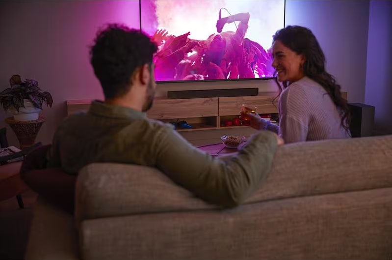 Couple sur un canapé regardant la télé, concert avec lumières, boissons et snacks.