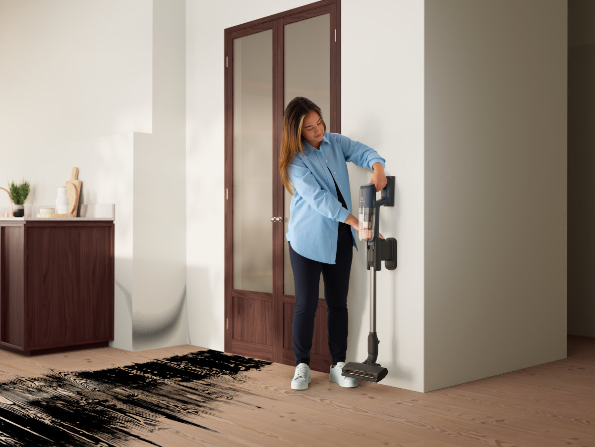 Kobieta umieszcza odkurzacz na uchwycie ściennym. Na podłodze jest czarna plama farby.