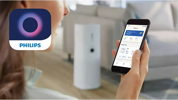 Egy nő, aki egy telefont tart a kezében, rajta a Philips app logójával, és egy okosotthon eszközzel.