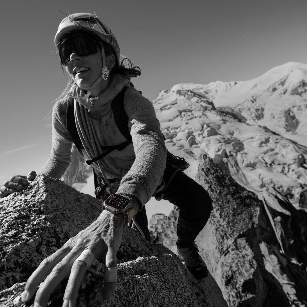 Kobieta wspinająca się po ścianie skalnej, nosząca Apple Watch, na czarno-białym zdjęciu.