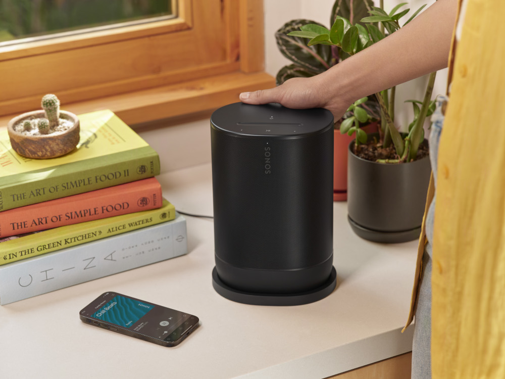 A black Sonos speaker next to a smartphone and books on a counter.