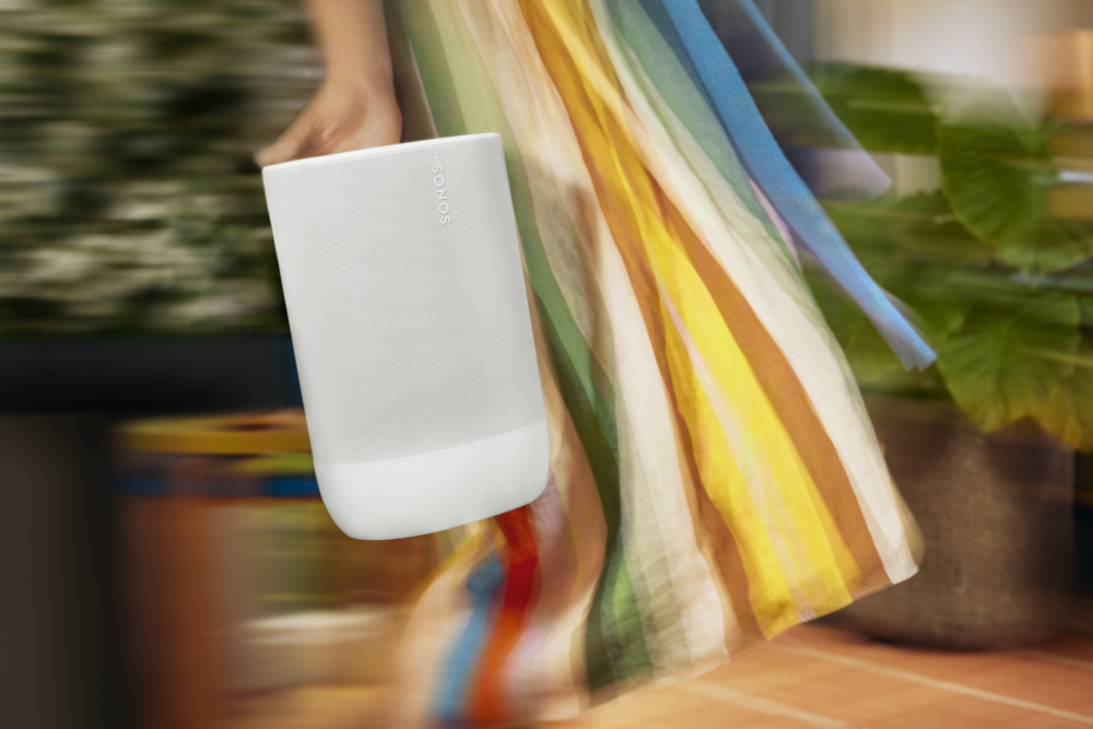 Een persoon in een zwierige jurk houdt een witte Sonos speaker vast, beweging wazig.