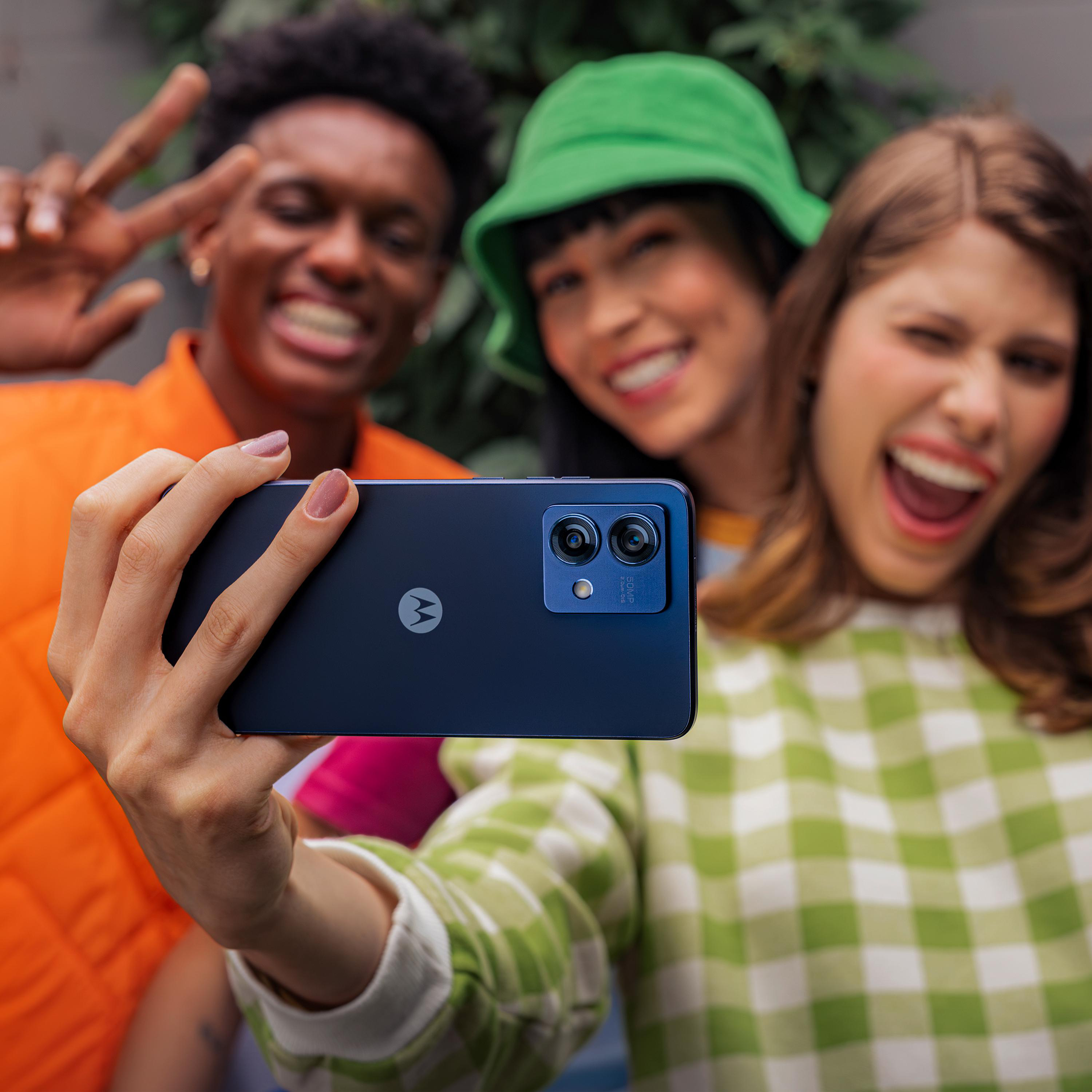 Drei Personen machen ein Selfie mit einem dunkelblauen Telefon. Einer zeigt Peace, andere lächeln.