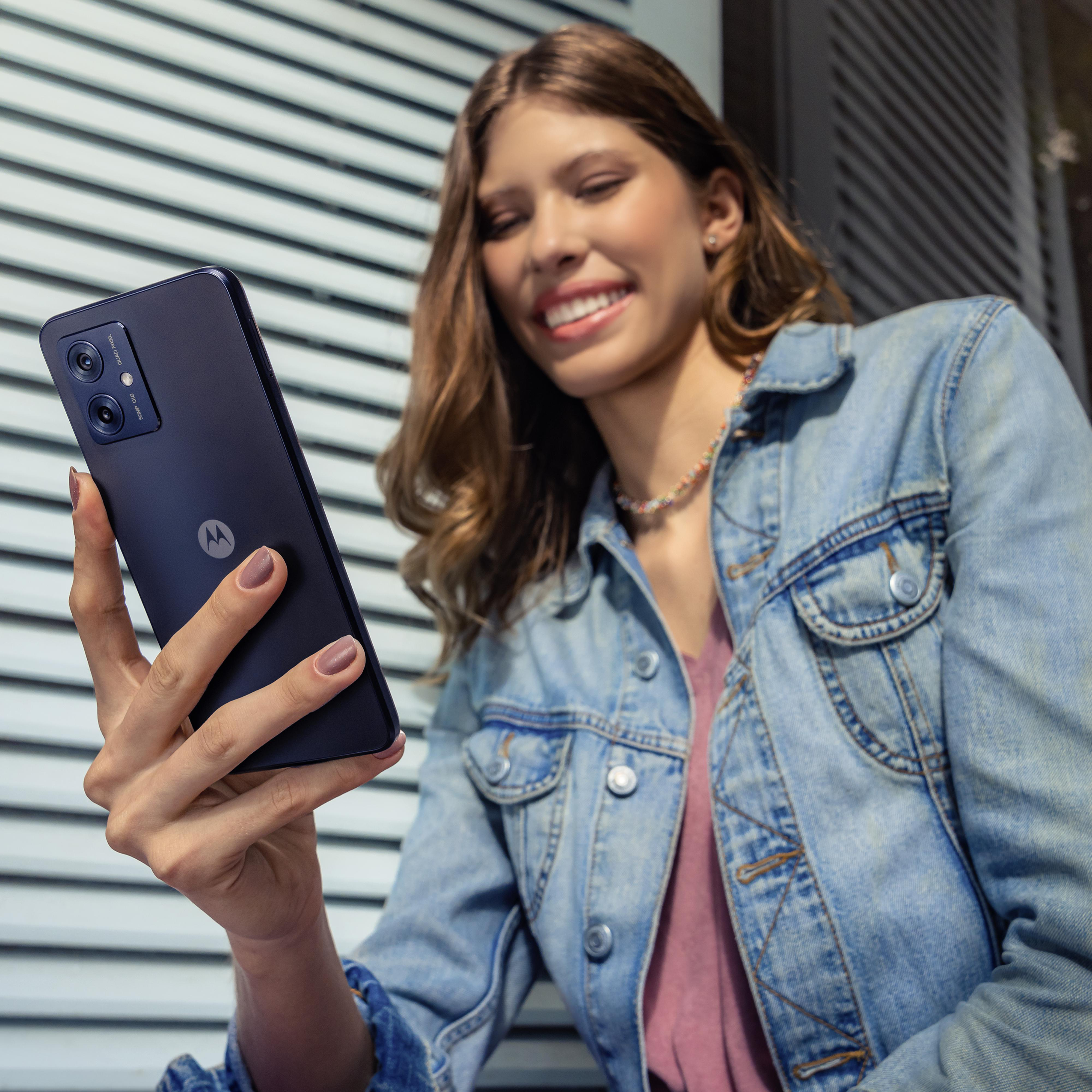 Eine Frau hält ein dunkelblaues Motorola-Telefon. Sie lächelt und trägt eine Jeansjacke.