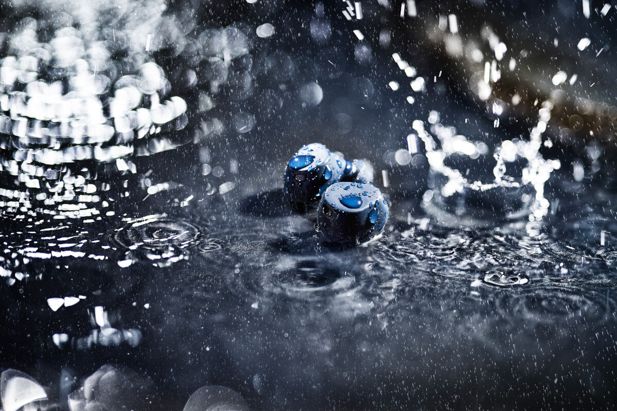 Niebieskie słuchawki w wodzie z rozpryskami, kroplami i zmarszczkami, ciemne tło.