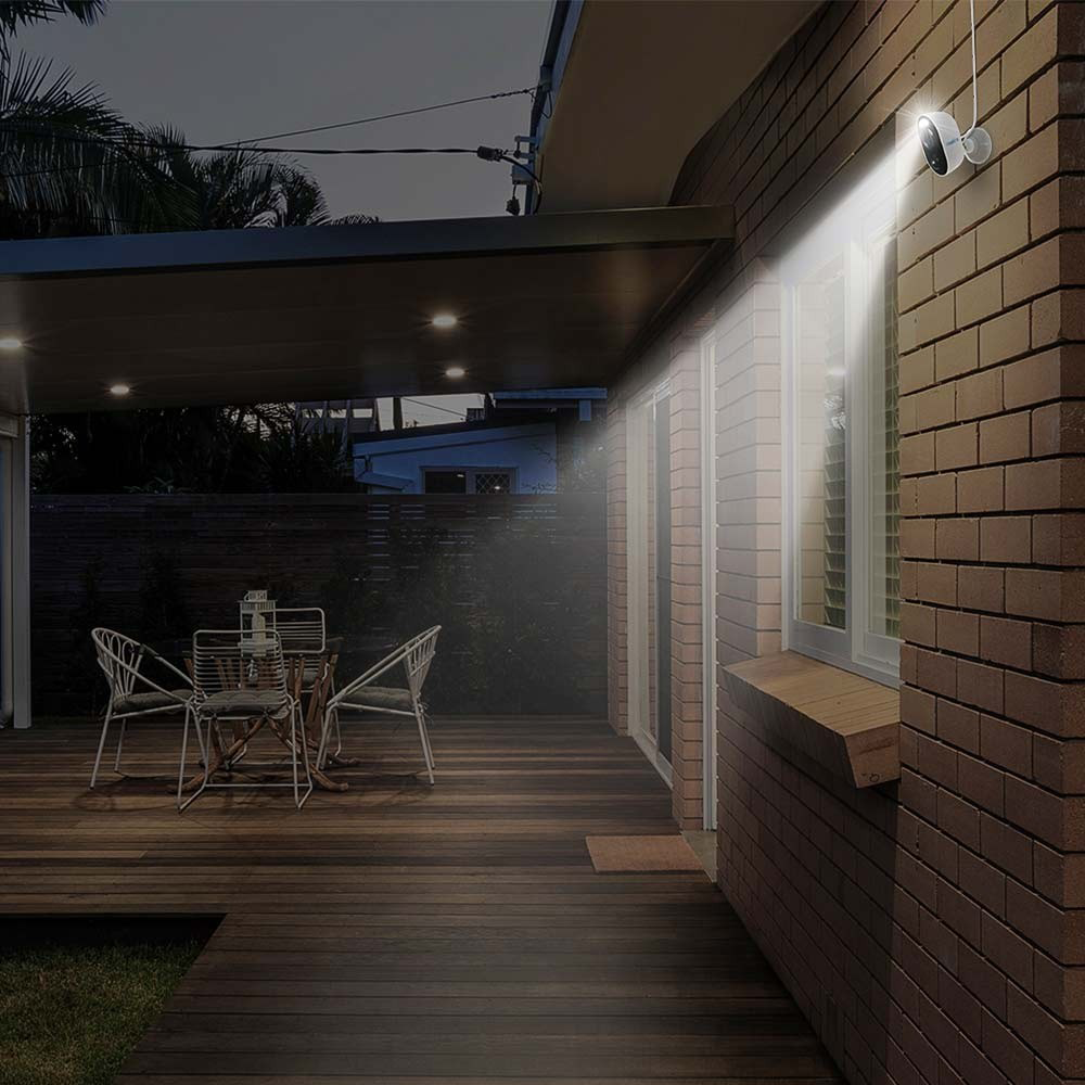 Außenaufnahme bei Nacht, Flutlicht beleuchtet Backsteinmauer und Deck. Tisch und Stühle stehen auf dem Deck. Haus im Hintergrund.