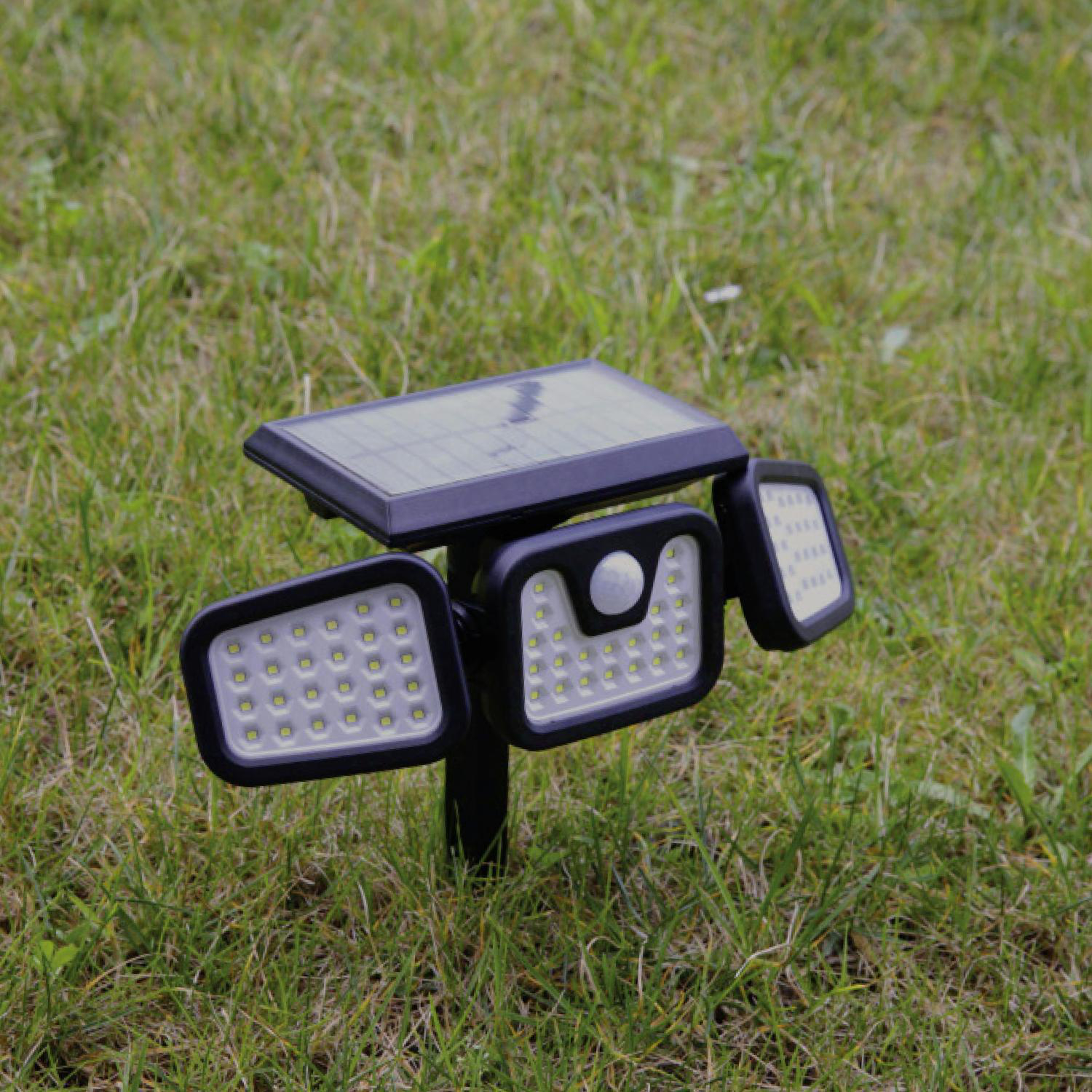 Eine solarbetriebene Außenleuchte. Sie hat drei Lichtpaneele und ist auf Gras platziert.