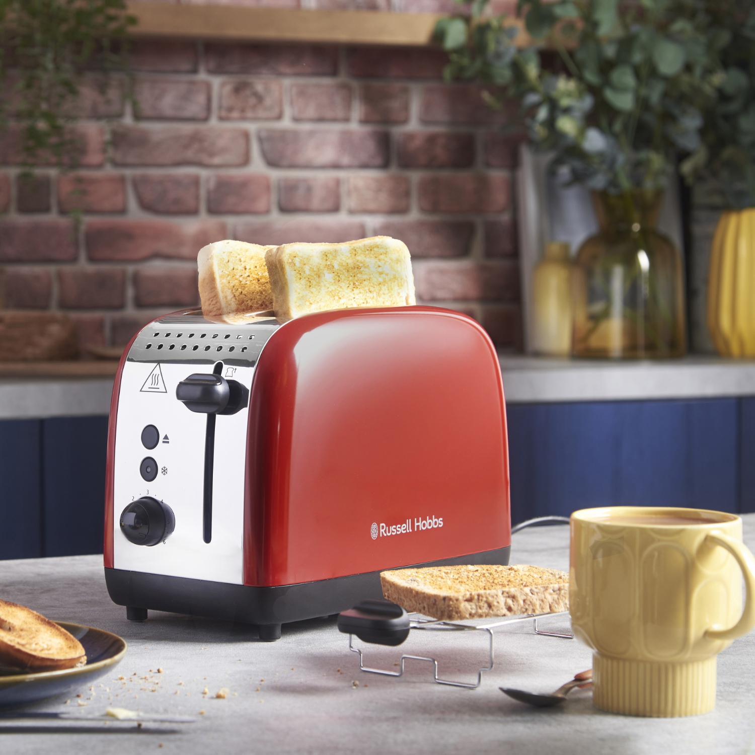 Red Russell Hobbs toaster with toast popping out. A yellow mug on the right.
