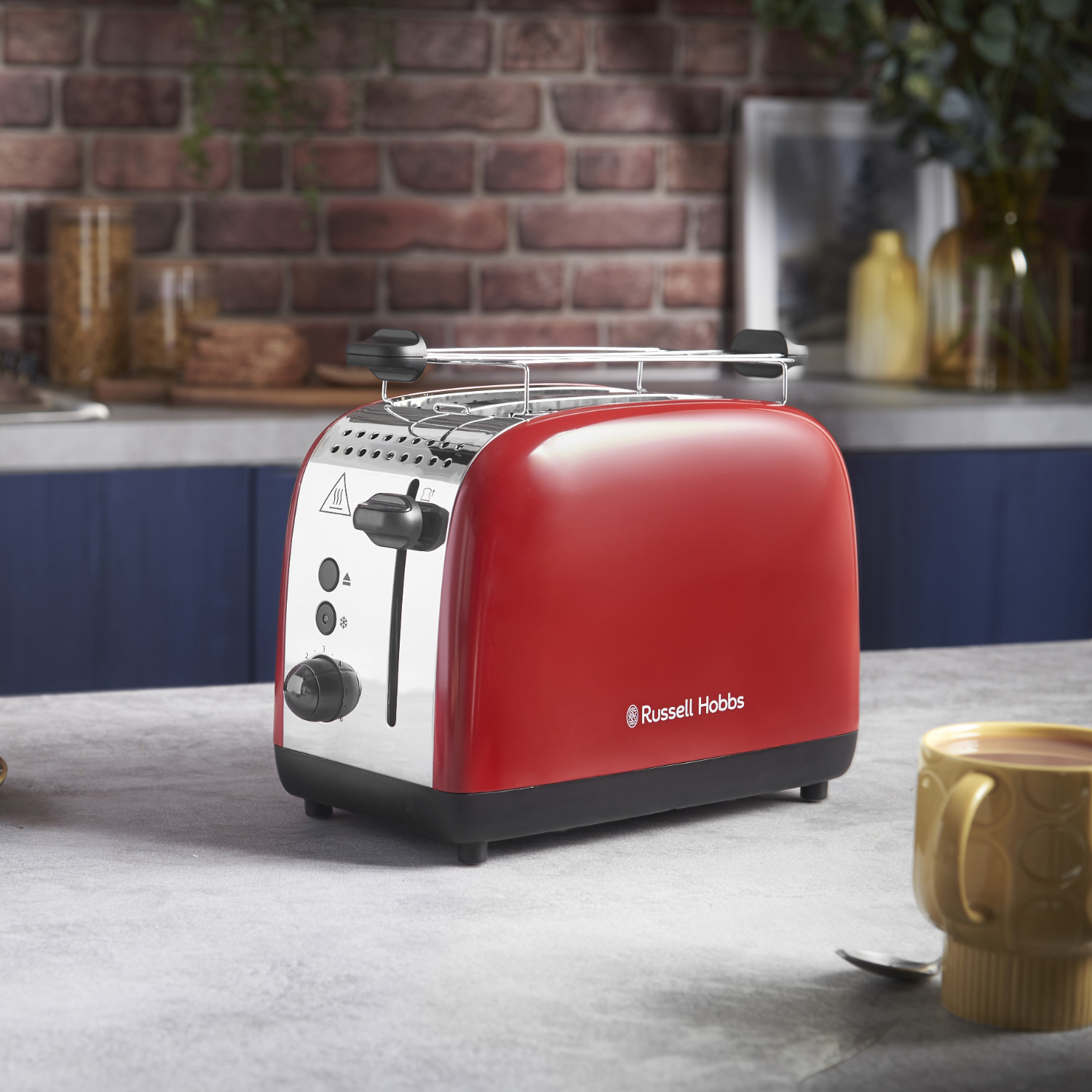 Red and silver toaster on a grey counter, with a yellow mug.