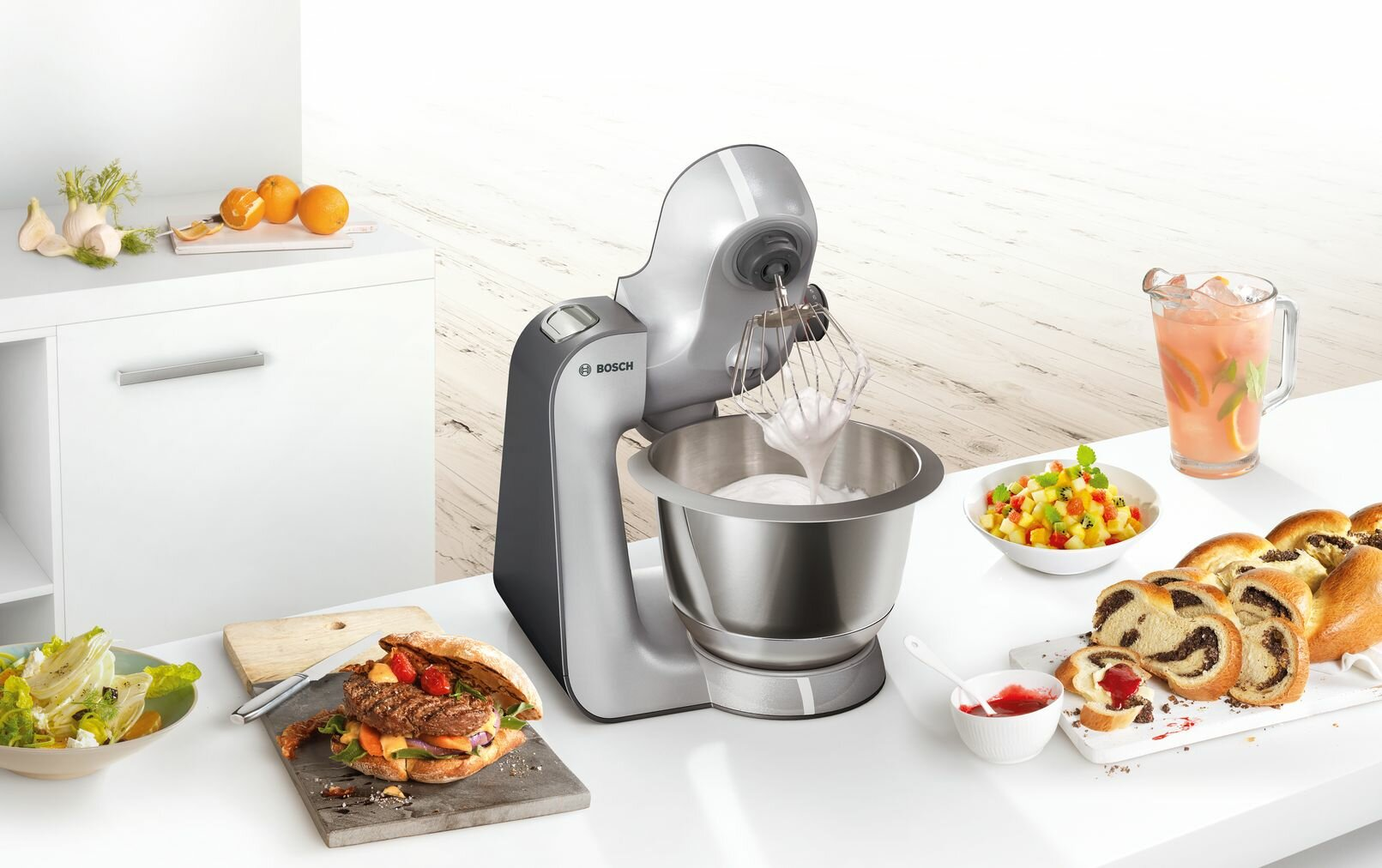 Scena kuchenna z mikserem, jedzeniem i składnikami na białym stole.