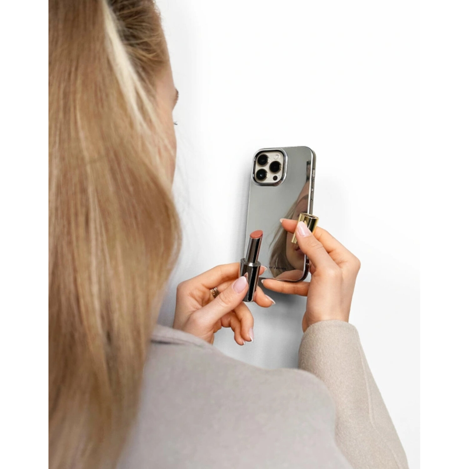Une femme appliquant du rouge à lèvres devant un iPhone miroir, tenant le téléphone et le rouge à lèvres.