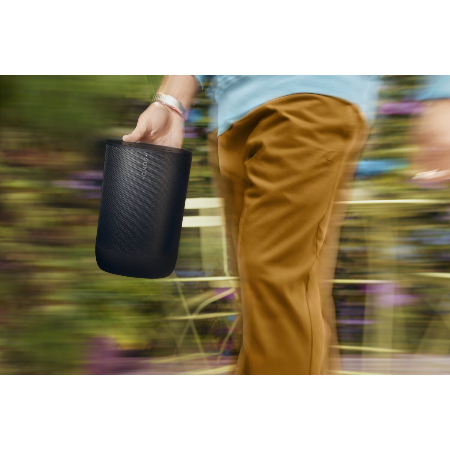 A person holding a black cylindrical speaker while walking outside.