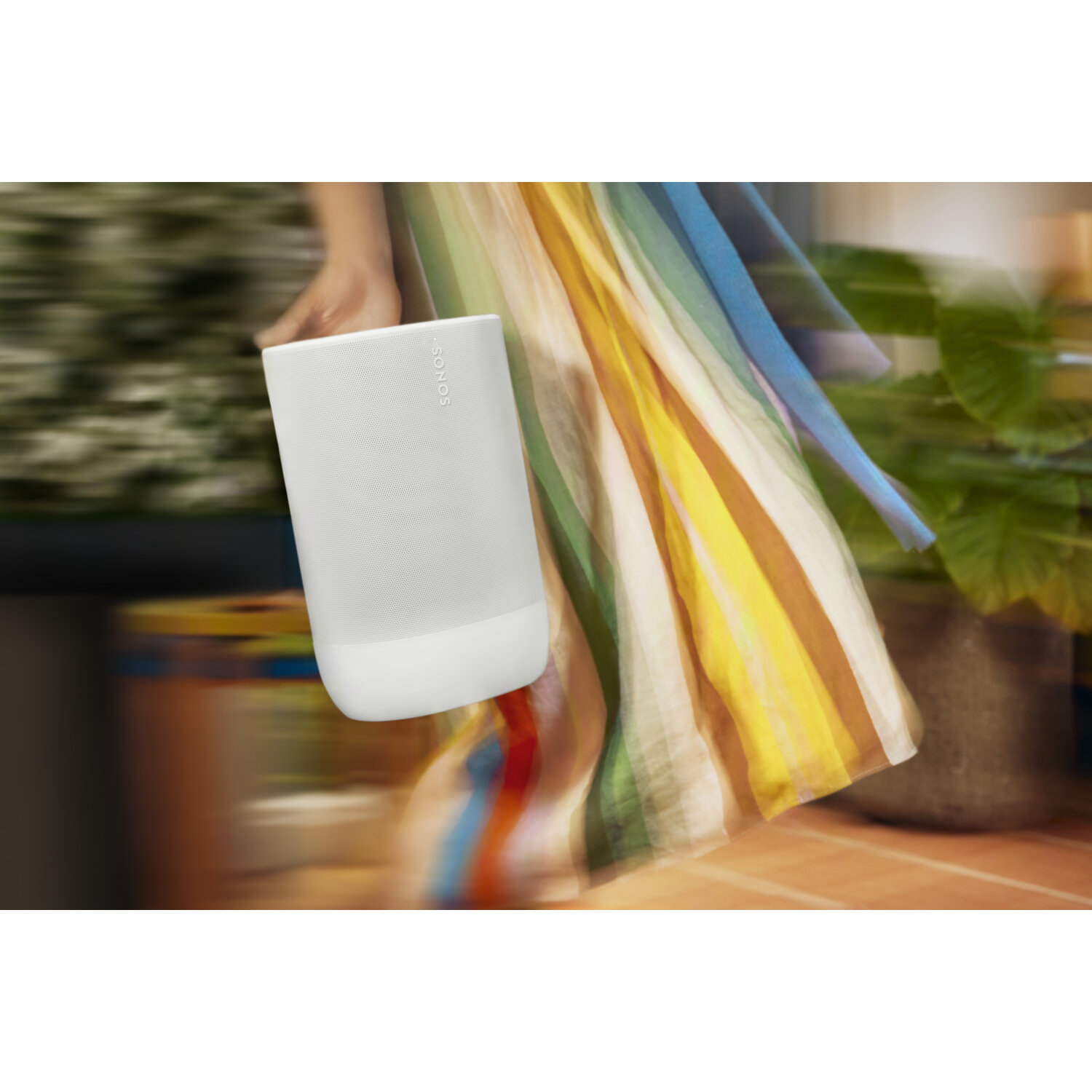 Een witte Sonos-luidspreker vastgehouden door een persoon met een kleurrijke jurk, wazige achtergrond.