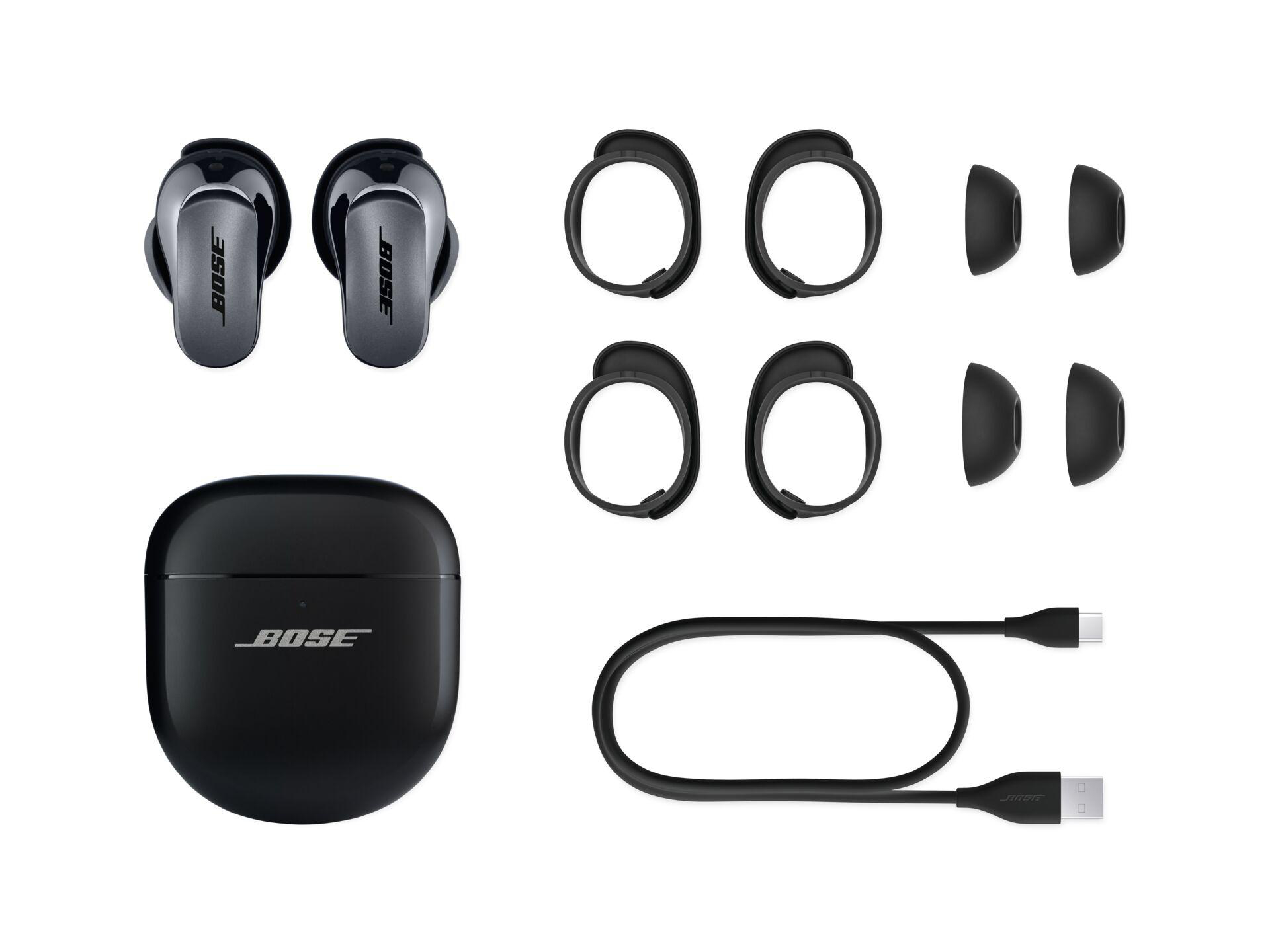Bose-Ohrhörer, Ladeetui und Zubehör auf weißem Hintergrund, alles schwarz.