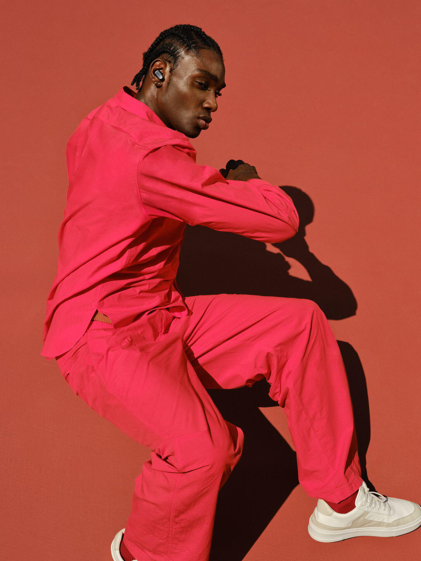 Mann in pinkfarbenem Outfit. Er springt mit Ohrhörern in den Ohren vor rotem Hintergrund.