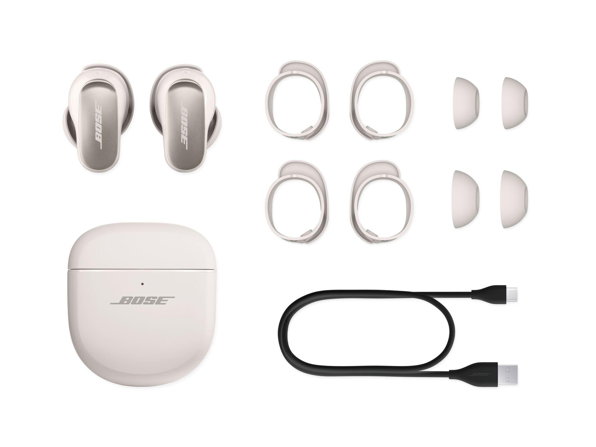 Bose-Ohrhörer, Ladecase, zusätzliche Ohrstöpsel und Ohrringe sowie ein Ladekabel, alles auf Weiß.